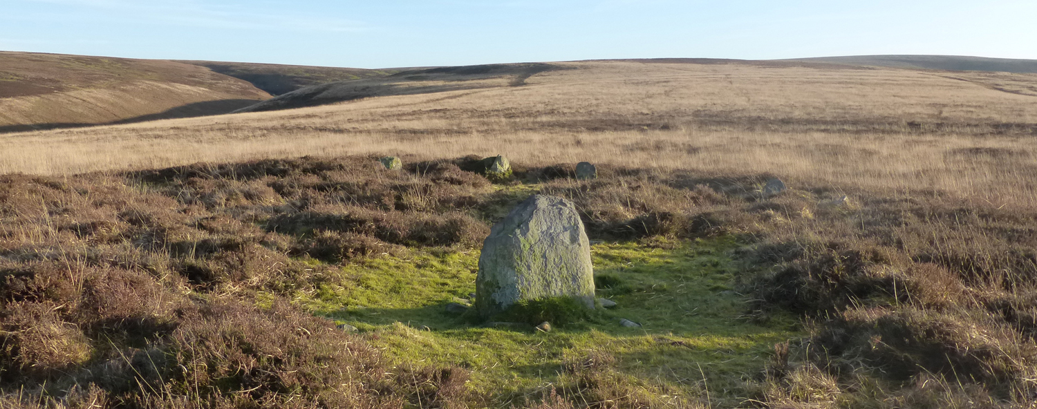 Cairn, bordered by more upright stones, set within a moorland landscape